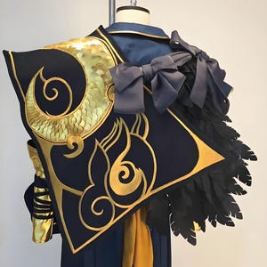 May include: A navy blue and gold cosplay costume with intricate detailing. The costume features gold embellishments, a black feather accent, and a large bow. The design includes a stylized golden spiral and flame motif.