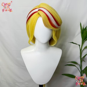 May include: A yellow wig with red and white stripes, styled with a side parting and soft curls. The wig is displayed on a white mannequin head. The Crazy Silk Party logo is visible in the top left and bottom right corners.