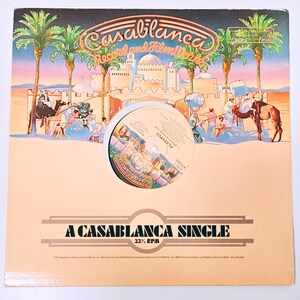 May include: A vintage vinyl record album cover with a desert scene featuring palm trees, camels, and a city skyline. The album is labeled "Casablanca Record and Filmworks" and "A Casablanca Single". The record label is visible in the center.
