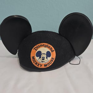 Può includere: Cappello nero con orecchie di Topolino. Il cappello in feltro presenta una toppa rotonda di Disneyland con Topolino. Un classico souvenir Disney.