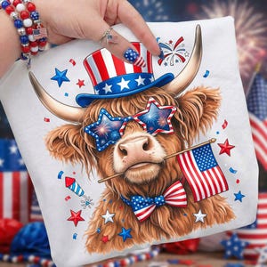 May include: White pillow featuring a Highland cow with patriotic accessories. The cow wears star-shaped sunglasses, a bow tie, and a top hat, all in red, white, and blue. It holds a small American flag in its mouth, with confetti and fireworks in the background.