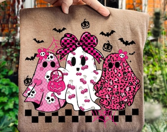 May include: A brown tote bag featuring three ghost illustrations in pink and white. The ghosts have floral and bow accents, with cherry and leopard print patterns. Black bats, pumpkins, and a checkered border complete the Halloween design.