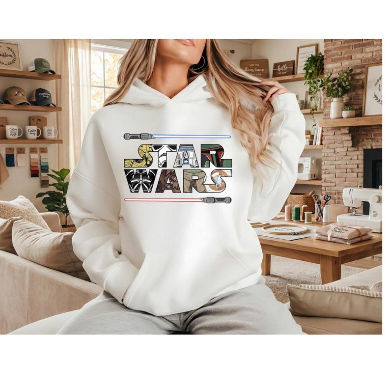 Puede incluir: Sudadera con capucha blanca con el texto "STAR WARS" en un dise&ntilde;o de letras de bloque colorido. El dise&ntilde;o incluye sables de luz arriba y abajo del texto. La sudadera es de estilo casual y c&oacute;modo.