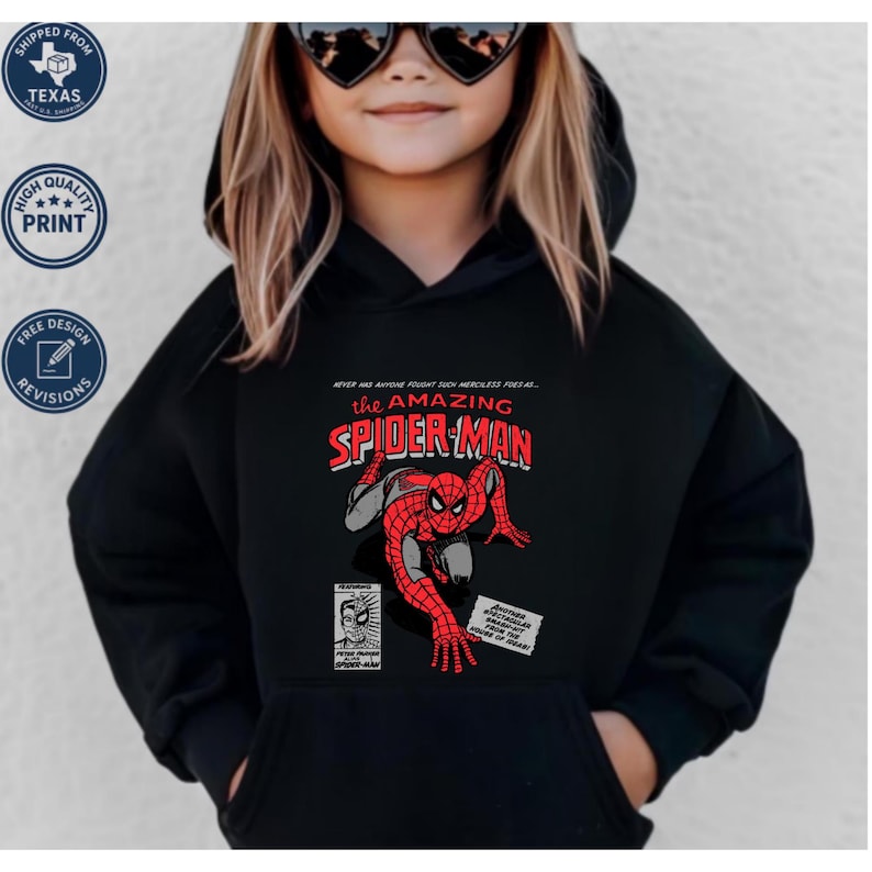 Puede incluir: Sudadera con capucha negra con un gr&aacute;fico de c&oacute;mic vintage de Spider-Man. El gr&aacute;fico incluye las palabras "THE AMAZING SPIDER-MAN" en rojo y blanco, con texto adicional y vi&ntilde;etas de c&oacute;mic. La sudadera tiene un bolsillo delantero.