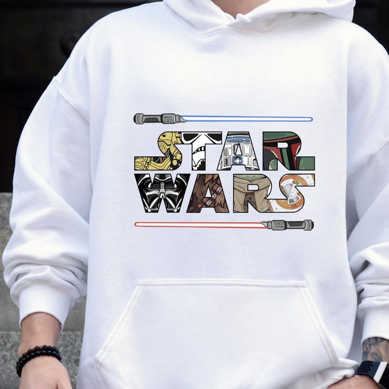 Puede incluir: Sudadera con capucha blanca con el texto "STAR WARS" en un dise&ntilde;o de letras en bloque colorido. El dise&ntilde;o incluye im&aacute;genes de personajes y sables de luz. La sudadera tiene un bolsillo delantero y una capucha con cord&oacute;n.