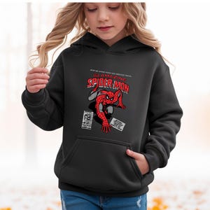 Puede incluir: Sudadera con capucha negra con un gr&aacute;fico de Spider-Man al estilo c&oacute;mic. El dise&ntilde;o incluye las palabras "The Amazing Spider-Man" en rojo y blanco, con texto adicional arriba y abajo del t&iacute;tulo. La sudadera tiene un bolsillo delantero.