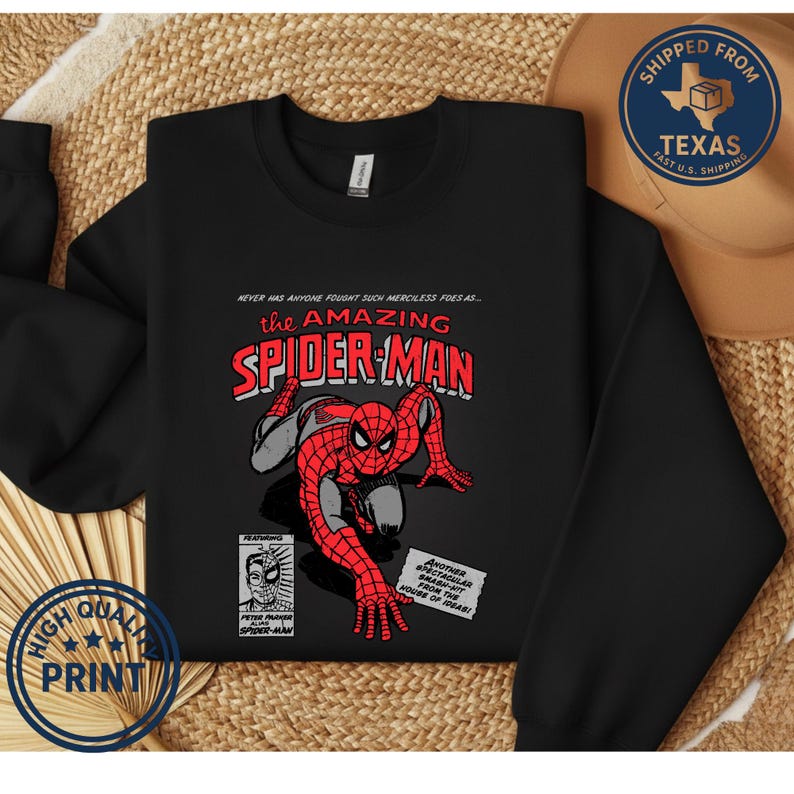Puede incluir: Sudadera negra con un dise&ntilde;o de c&oacute;mic vintage de Spider-Man. El gr&aacute;fico incluye las palabras "the AMAZING SPIDER-MAN" en rojo y blanco, con una ilustraci&oacute;n detallada del superh&eacute;roe. La camisa tambi&eacute;n tiene el texto "HIGH QUALITY PRINT".