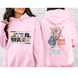 Puede incluir: Sudadera con capucha rosa claro con el logotipo de Star Wars en la parte delantera y un gr&aacute;fico en la parte trasera. El dise&ntilde;o frontal incluye el texto Star Wars con sables de luz. El gr&aacute;fico trasero presenta a Darth Vader, un Stormtrooper y la Estrella de la Muerte.