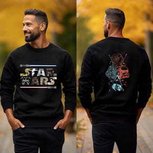 Puede incluir: Sudadera negra con el logo de Star Wars, sables de luz e ilustraciones de personajes. La parte trasera de la sudadera muestra un gr&aacute;fico de varios personajes de Star Wars. La sudadera se muestra en una persona.