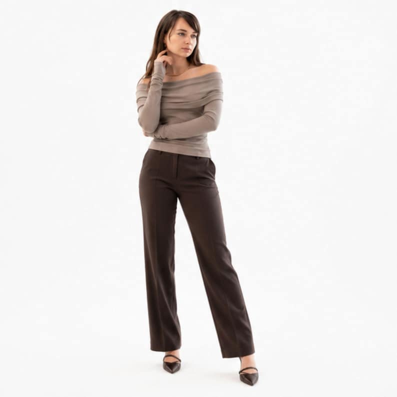 Pu&ograve; includere: Una donna indossa un top color talpa con spalle scoperte e maniche lunghe e pantaloni a gamba larga marrone scuro. L'outfit &egrave; abbinato a tacchi neri a punta. Lo sfondo &egrave; bianco.