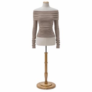 Pu&ograve; includere: Un top color talpa con spalle scoperte e maniche lunghe esposto su un manichino. Il top ha un corpetto arricciato e maniche aderenti. Il manichino &egrave; su un supporto in legno con base rotonda, su sfondo bianco.