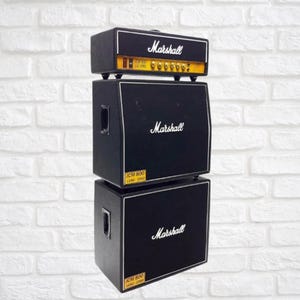 May include: A black Marshall JCM 800 guitar amplifier stack. The stack comprises a head and two speaker cabinets. The head features gold knobs and the Marshall logo. The cabinets also display the Marshall logo and the text "JCM 800 LEAD 1960".