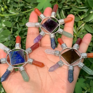 Peut inclure: Trois générateurs d'énergie en cristal avec une pierre précieuse centrale et des pointes de cristal rayonnantes de différentes couleurs. Chaque générateur a un cadre en métal argenté. Le fond est un feuillage vert flou.