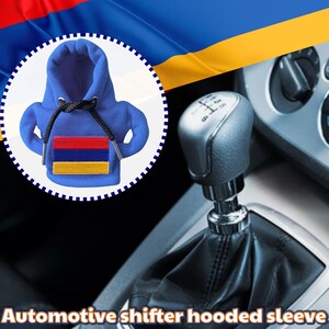 Könnte beinhalten: Ein blauer Schalthebel-Hoodie im Miniatur-Hoodie-Design mit der armenischen Flagge. Der Schalthebel hat einen schwarzen Kordelzug und befindet sich vor einem Autoinnenraum und der armenischen Flagge.