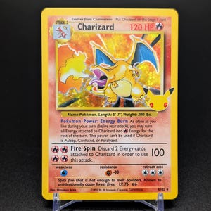 Puede incluir: Una carta de Pokémon Charizard, con una criatura con forma de dragón amarillo y naranja con alas azules. La carta tiene texto que incluye "Charizard", "120 HP" y "Fire Spin". La carta está sobre un soporte de plástico transparente.