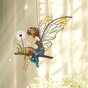May include: A stained glass fairy ornament, featuring a seated fairy with brown hair and a floral crown, holding a dandelion. The fairy is wearing a colorful dress and has large, stained glass wings. The ornament hangs from a chain.
