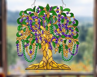Puede incluir: Un atrapasoles con forma de árbol de estilo vidriera con hojas verdes, cuentas moradas y doradas y un tronco amarillo. El atrapasoles está hecho de acrílico y cuelga de una cadena plateada.