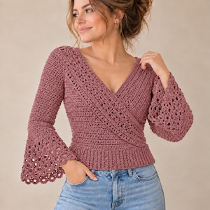May include: A dusty rose crochet wrap top featuring a deep V-neckline, long sleeves with flared, open-work lace cuffs, and a ribbed hem. The garment is crafted with a textured stitch pattern and is paired with light blue denim jeans.