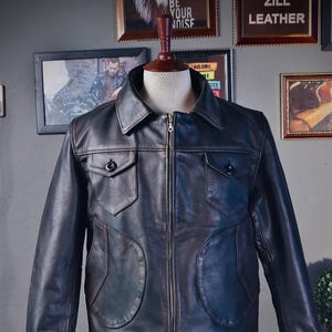 Puede incluir: Una chaqueta de cuero azul oscuro con cierre de cremallera y varios bolsillos. La chaqueta tiene cuello y mangas largas.