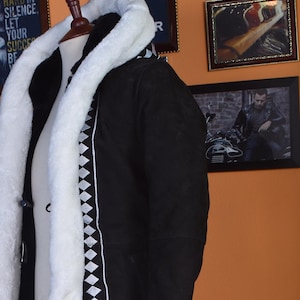 May include: A black hooded winter coat with a white fur trim and a diamond pattern design on the sleeves and sides.