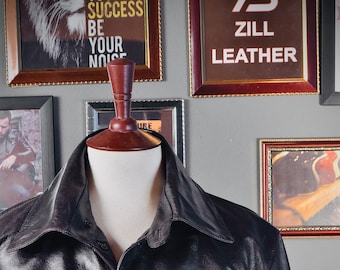 May include: A black leather jacket with a button-up front and a collar. The jacket has a pocket on the left chest and two pockets on the bottom.