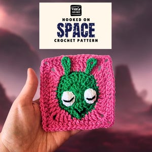 May include: A crocheted square featuring a green alien face with white eyes on a pink background. The text "HOOKED ON SPACE CROCHET PATTERN" is displayed above the square. The Yarn Square logo is in the top left corner.
