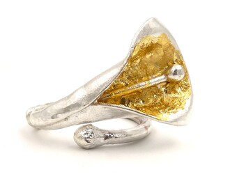 May include: A silver ring with a gold flower design. The flower is a calla lily with a textured surface. The ring is open and adjustable.