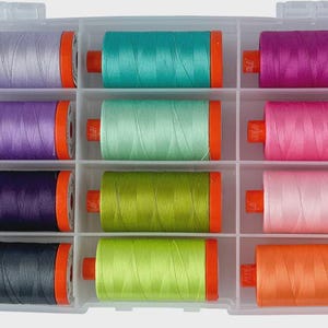 May include: A clear plastic organizer filled with twelve spools of colorful thread. The thread colors include shades of purple, teal, green, pink, and orange. Each spool has orange end caps. Ideal for sewing and crafting projects.
