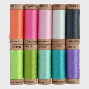 May include: A collection of colorful Aurifil thread spools. The spools are arranged in two rows, showcasing a variety of vibrant colors including orange, pink, light pink, white, dark gray, green, light green, teal, turquoise, and purple. Each spool has a wooden base and top.