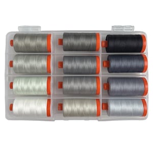 May include: A clear plastic storage case containing twelve spools of sewing thread arranged in a grid. The spools feature various shades of gray, white, and black thread, each wound on a cylinder with bright orange plastic end caps.
