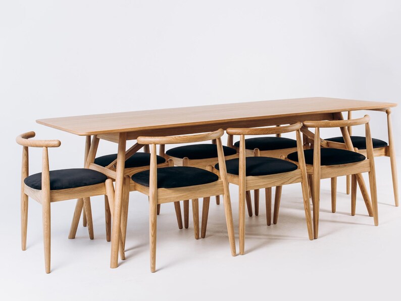 May include: A light wood dining table with six matching chairs. The chairs have black cushioned seats and curved backs. The table and chairs are set against a white background, showcasing a minimalist design.