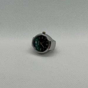May include: A silver ring watch with a dark green face and black Roman numeral hour markers. The watch face has the brand name "BOZHI" printed on it. The ring is a unique accessory.