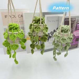 Può includere: Tre portavasi sospesi all'uncinetto con foglie verdi e un vaso color crema. I portavasi sono appesi a uno spago bianco.