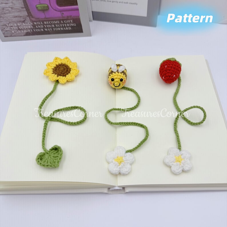 May include: Crocheted bookmarks in the shape of a sunflower, bee, and strawberry. Each bookmark has a green stem and a white flower or green leaf. The word "Pattern" is visible in the image.