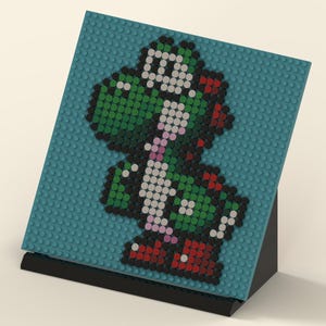 Könnte beinhalten: Pixel-Art-Darstellung von Yoshi aus der Super Mario-Videospielserie. Das Kunstwerk besteht aus kleinen, farbigen Blöcken auf einer türkisfarbenen Basis, die auf einem schwarzen Ständer montiert sind. Yoshi ist in Grün, Weiß, Rot und Rosa dargestellt.
