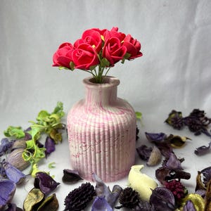 Op de afbeelding: Een kleine roze en witte marmeren keramische vaas met een boeket felroze viltrozen.