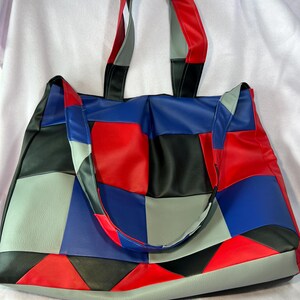 Peut inclure: Un grand sac fourre-tout en patchwork avec un motif bleu, rouge, noir et gris. Le sac a deux longues anses et une base large.