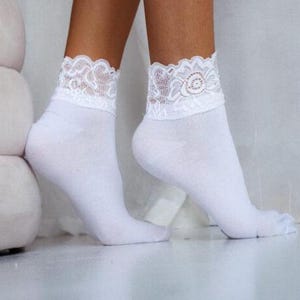 Pode incluir: Meias brancas de tornozelo com uma borda de renda branca ao redor da parte superior da meia.