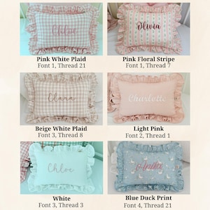 May include: A collection of decorative pillows with ruffled edges. The pillows come in various colors and patterns, including pink plaid, floral stripes, and a blue duck print. Each pillow features a personalized name embroidered in a matching thread color.