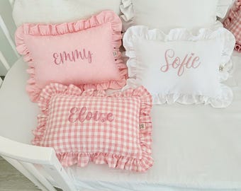 Può includere: Tre cuscini rettangolari con bordi a volant. Uno è rosa a pois bianchi con il nome Emmy ricamato in rosa. Uno è bianco con il nome Sofie ricamato in rosa. Uno è a quadretti vichy rosa e bianchi con il nome Eloise ricamato in rosa.
