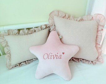 May include: Three pink pillows with ruffled edges. The star-shaped pillow has the name "Olivia" embroidered on it.