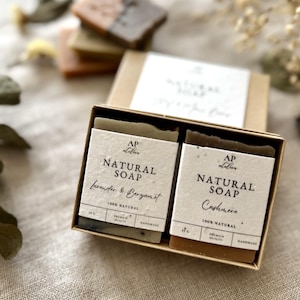 May include: A gift box containing two bars of natural soap, one labeled "Lavender & Bergamot" and the other "Cashmere." The soaps are rectangular and light green and brown. The box is beige with a white label.