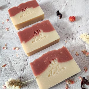 Può includere: Tre saponette fatte a mano con un design a spirale rosa e bianco. Il sapone è timbrato con le lettere "AP" e la parola "atelier".