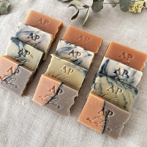 May include: A collection of small, rectangular bars of soap with a variety of colors and patterns. Each bar has the letters "AP atelier" embossed on it.