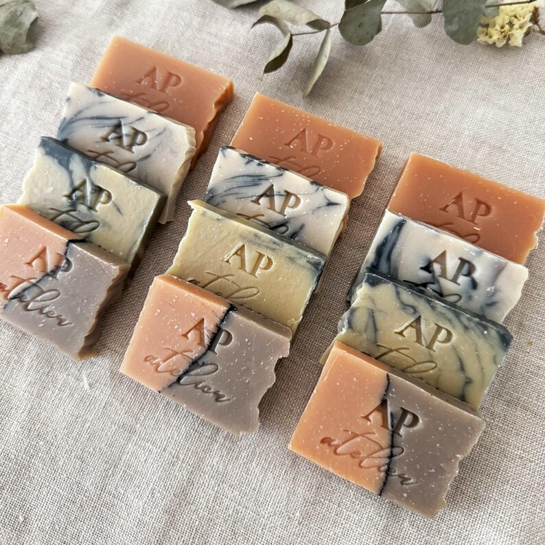 May include: A collection of small, rectangular bars of soap with a variety of colors and patterns. Each bar has the letters "AP atelier" embossed on it.