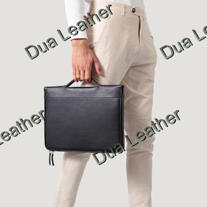 May include: A black leather briefcase with a handle and zipper closure. The briefcase is held by a person wearing beige pants and a white shirt. The text "Dua Leather" is visible on the image.