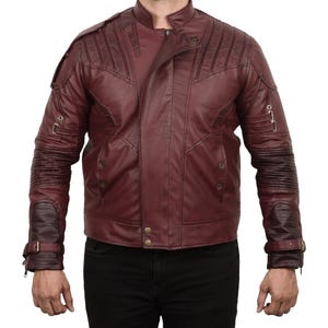 May include: A maroon leather jacket with a zip closure and a stand-up collar. The jacket has a quilted design on the sleeves and a zipped pocket on the left sleeve.