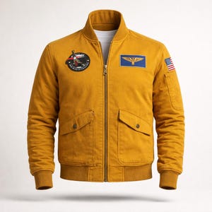 May include: Mustard yellow bomber jacket with a ribbed collar, cuffs, and hem. Features a zipper closure, two front pockets, and several patches, including an American flag patch on the right sleeve. The jacket has a quilted lining.