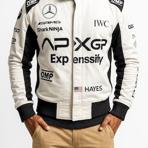 May include: Cream-colored racing jacket with black accents and multiple sponsor logos, including "AMG", "Shark NINJA", and "APXGP". Features a stand-up collar, ribbed cuffs, and the text "HAYES" with a small American flag.