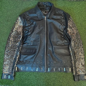 May include: A black leather jacket with silver studs on the sleeves and a zip closure. The jacket has a label that reads "Real Leather".